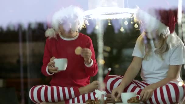 クリスマスの帽子をかぶった2人の子供が座って お茶を飲み クリスマスの時間に家でケーキを食べる — ストック動画