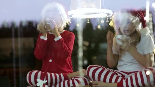 Two Kids Wearing Christmas Hats Sitting Drinking Tea Home Christmas — 图库视频影像