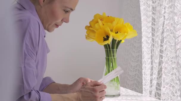 Woman in her 40s observes the presented flowers and a handmade card. — Wideo stockowe