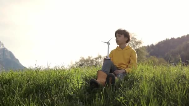 Niño vestido con capucha amarilla mantiene modelo de turbina eólica. — Vídeo de stock