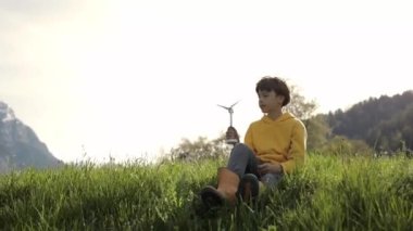 Boy dressed in yellow hoodie keeps model wind turbine.