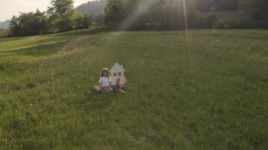 Sister and the brother are keeping paper house and mini wind turbine. Slow motion