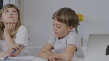 Boy of 9 years old helps his younger sister to make her homework. High quality 4k footage
