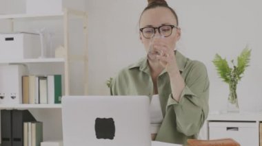 Young female between 30 and 40 years old drinks water in front of pc. 