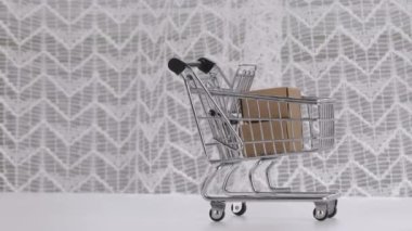 Mini shopping cart and small carton boxes in it on a white table. Negative space
