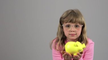 Caucasian girl of 7 years with yellow piggy bank. High quality 4k footage