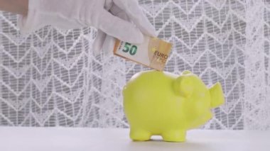 Beyaz pamuk eldivenli insan eli domuz kumbarasına 50 euro yatırıyor. Yakın çekim.
