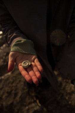a girl on the seashore, in a long raincoat. holds a shell in his hand