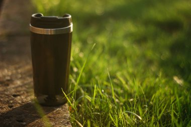 a thermos for hot drinks on a hike or a walk in the park. a thermos on the background of the sunset in the garden.