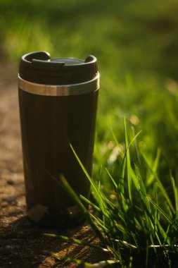 a thermos for hot drinks on a hike or a walk in the park. a thermos on the background of the sunset in the garden.