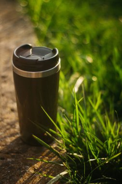 a thermos for hot drinks on a hike or a walk in the park. a thermos on the background of the sunset in the garden.