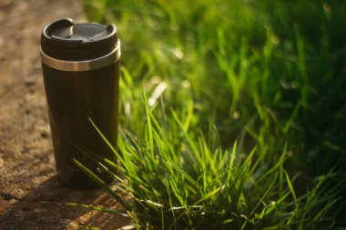 a thermos for hot drinks on a hike or a walk in the park. a thermos on the background of the sunset in the garden.