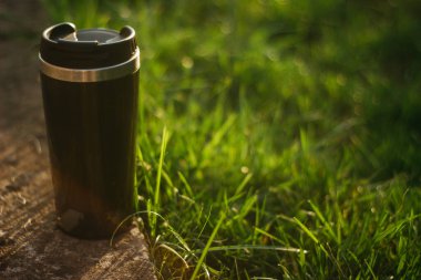 a thermos for hot drinks on a hike or a walk in the park. a thermos on the background of the sunset in the garden.