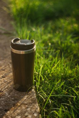 a thermos for hot drinks on a hike or a walk in the park. a thermos on the background of the sunset in the garden.