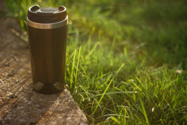 a thermos for hot drinks on a hike or a walk in the park. a thermos on the background of the sunset in the garden.