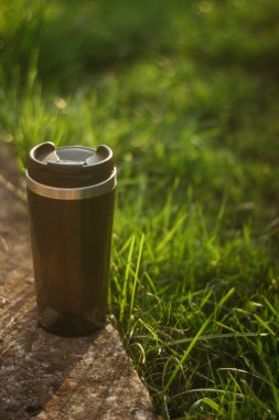 a thermos for hot drinks on a hike or a walk in the park. a thermos on the background of the sunset in the garden.