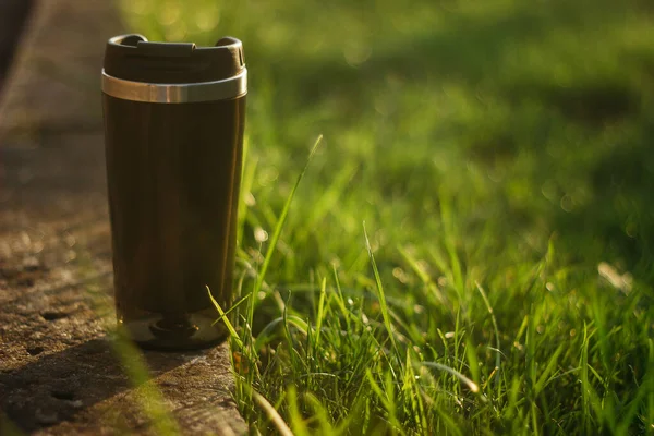 a thermos for hot drinks on a hike or a walk in the park. a thermos on the background of the sunset in the garden.