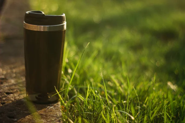 a thermos for hot drinks on a hike or a walk in the park. a thermos on the background of the sunset in the garden.