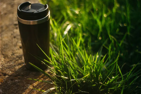 a thermos for hot drinks on a hike or a walk in the park. a thermos on the background of the sunset in the garden.