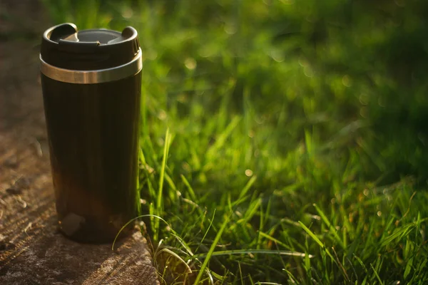 a thermos for hot drinks on a hike or a walk in the park. a thermos on the background of the sunset in the garden.