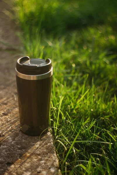 a thermos for hot drinks on a hike or a walk in the park. a thermos on the background of the sunset in the garden.