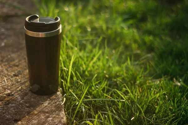 a thermos for hot drinks on a hike or a walk in the park. a thermos on the background of the sunset in the garden.