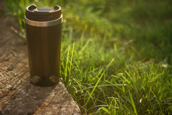 a thermos for hot drinks on a hike or a walk in the park. a thermos on the background of the sunset in the garden.