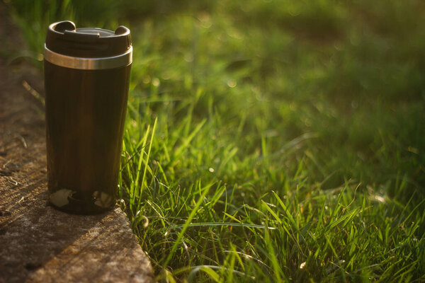 a thermos for hot drinks on a hike or a walk in the park. a thermos on the background of the sunset in the garden.