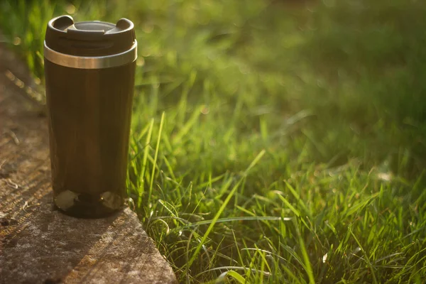 a thermos for hot drinks on a hike or a walk in the park. a thermos on the background of the sunset in the garden.