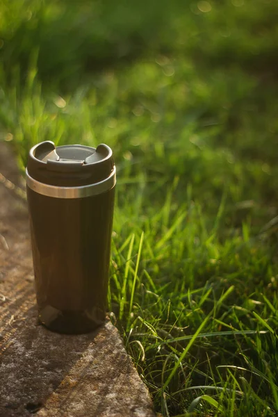 a thermos for hot drinks on a hike or a walk in the park. a thermos on the background of the sunset in the garden.