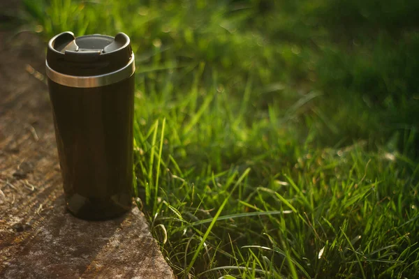 a thermos for hot drinks on a hike or a walk in the park. a thermos on the background of the sunset in the garden.
