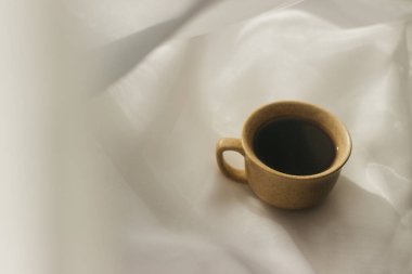 Sabahları bir fincan kahve. Espresso kahvesi. Beyaz bir bez üzerinde beyaz fincanlı kahve fincanı üzerine kahve lapası. Bir fincan kahveye güneş ışığı.