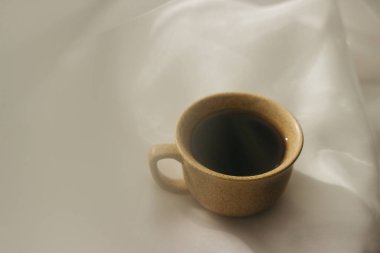Sabahları bir fincan kahve. Espresso kahvesi. Beyaz bir bez üzerinde beyaz fincanlı kahve fincanı üzerine kahve lapası. Bir fincan kahveye güneş ışığı.