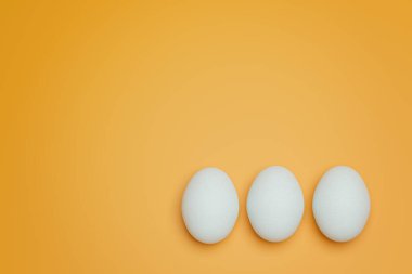 Sarı arka planda üç beyaz tavuk yumurtası. Yaratıcı gıda minimalist arka plan.