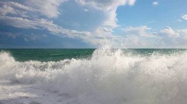 Dalgalı, köpüklü ve gökyüzünde güzel bulutlu turkuaz deniz.