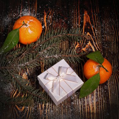 Mandalinaların, köknar ağacının dallarının ve kahverengi ahşap karla kaplı beyaz hediye kutusunun Noel bileşimi