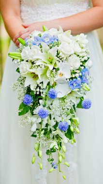 Gelinin ellerinde mavi ve beyaz çiçeklerden oluşan güzel bir düğün buketi. Seçici odak