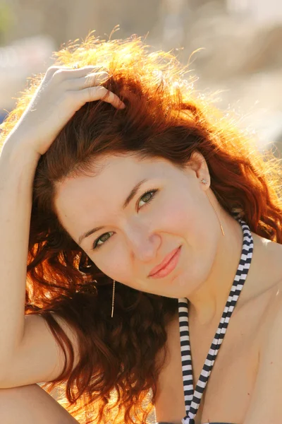 Gyönyörű fiatal vöröshajú nő mosolyogva, és fogta a kezét a haja — Stock Fotó
