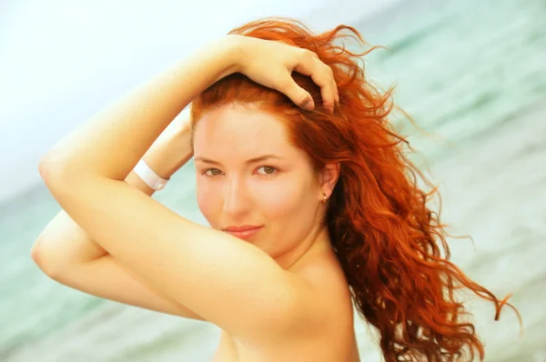 Vackra unga rödhårig kvinna ler och håller händerna i håret — Stockfoto