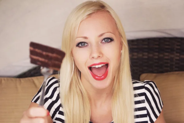 gülümseyen ve çikolatalı kek parçasını elinde tutan mutlu güzel sarışın kadın