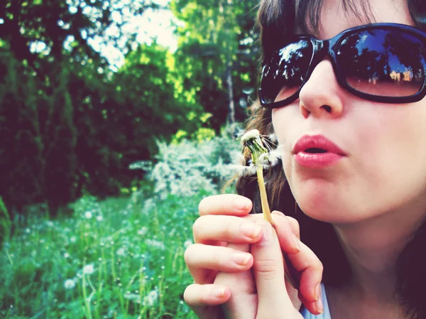 Una mujer guapa con gafas de sol soplando diente de león —  Fotos de Stock