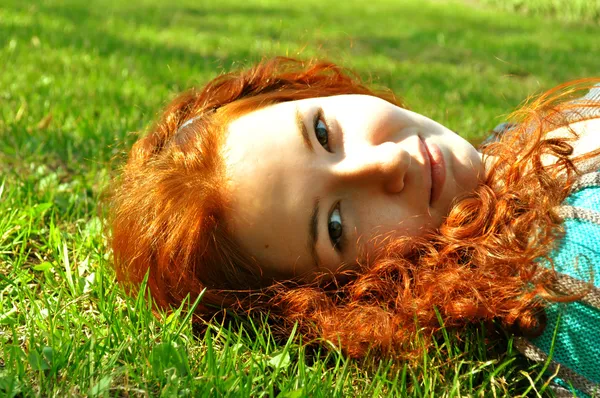 Una pelirroja bonita y feliz tumbada sobre hierba verde y sonriente —  Fotos de Stock
