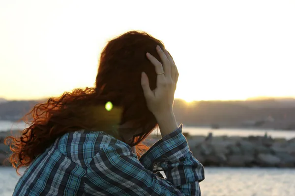 düşünceli genç kadın Kızıl saçlı bakarak günbatımı ve su