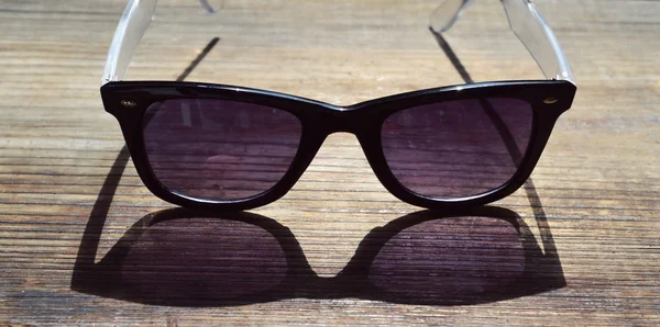 Lunettes de soleil noires avec verres violets sur une table en bois gros plan — Photo