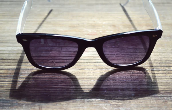 Lunettes de soleil noires avec verres violets sur une table en bois gros plan — Photo