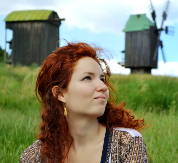 Beautiful young redhead woman looking away and thinking on the background of the mills — Stock Photo, Image