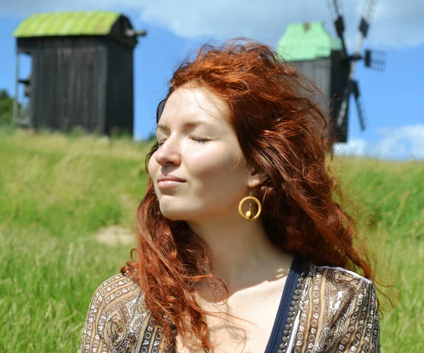 Belle jeune rousse souriante aux yeux fermés sur le fond des moulins — Photo