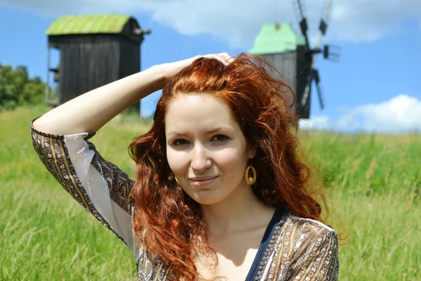 Bella giovane donna rossa sorridente e tenendo le mani tra i capelli sullo sfondo dei mulini — Foto Stock