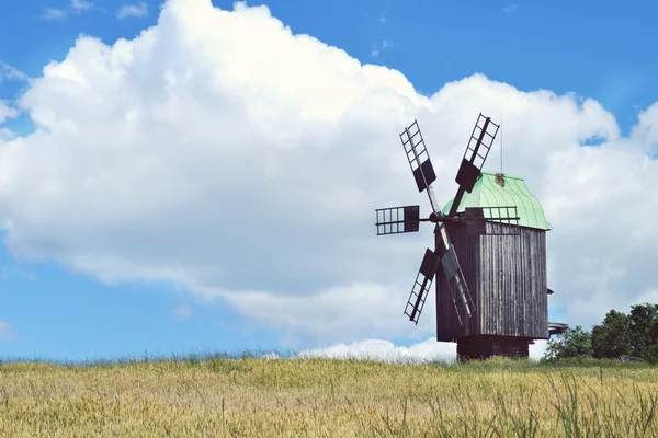 Velho moinho de vento de madeira em campo verde sobre céu azul brilhante e nuvens — Fotografia de Stock