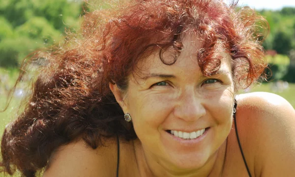 Mujer hermosa feliz con el pelo rojo en sus cuarentas oliendo al aire libre — Foto de Stock